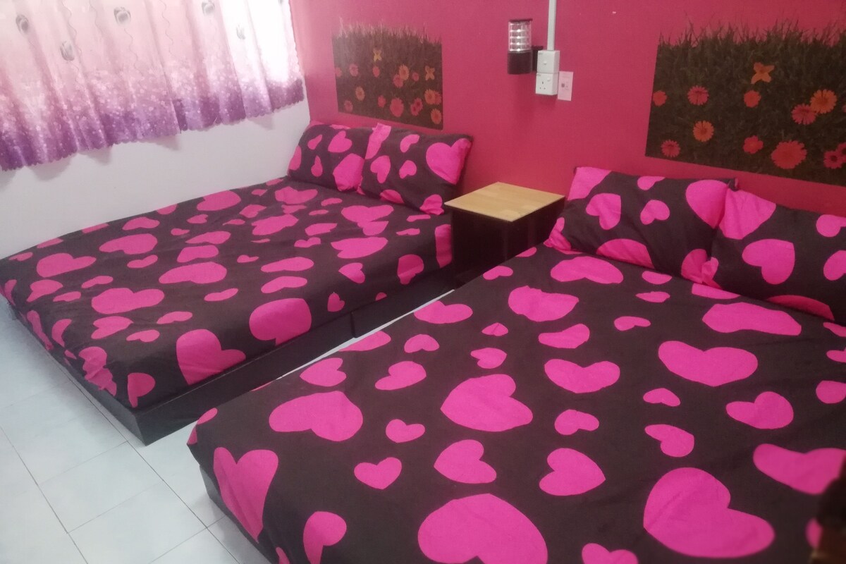Habitación con dos camas, cada una con una colcha marrón oscuro adornada con grandes corazones rosados.