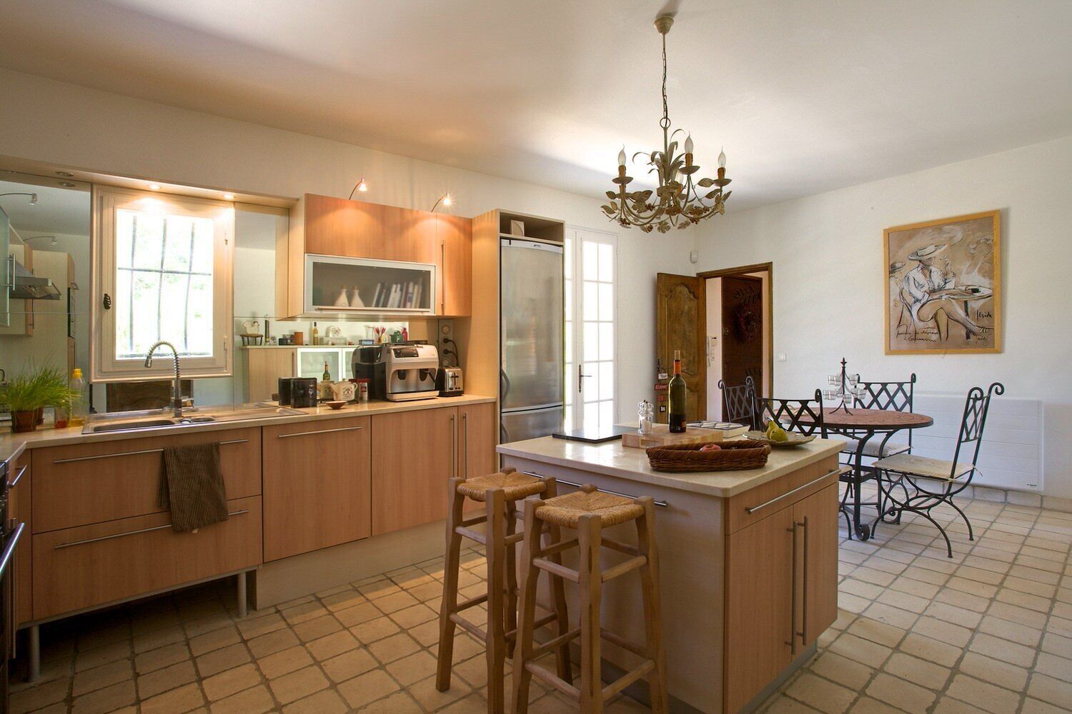 A modern kitchen with wooden cabinets, a central island, bar stools, and a dining table with chairs.