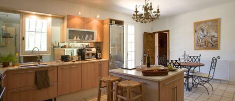 A modern kitchen with wooden cabinets, a central island, bar stools, and a dining table with chairs.