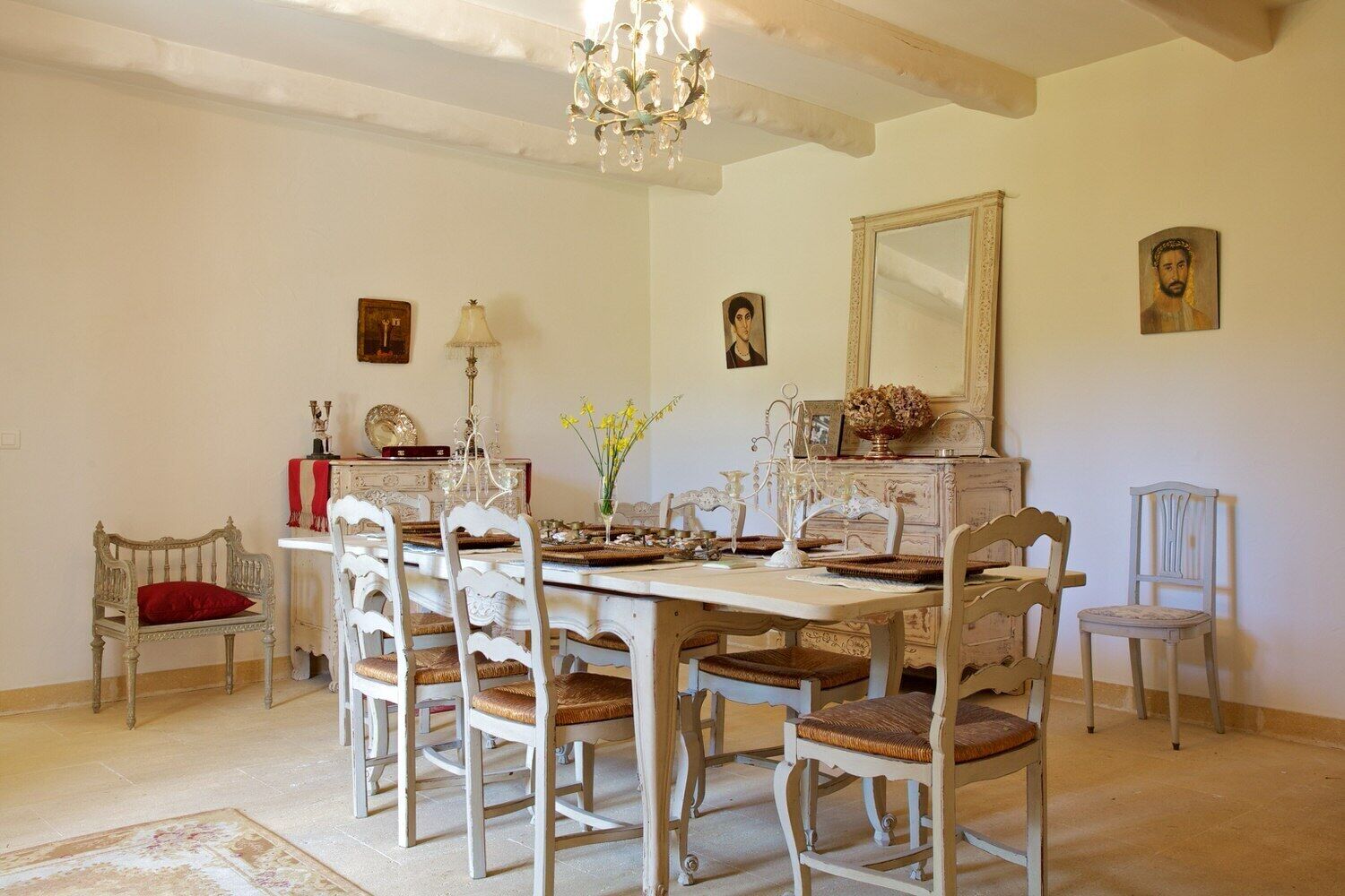 A dining room with a white table and chairs, a chandelier, and a mirror on the wall.