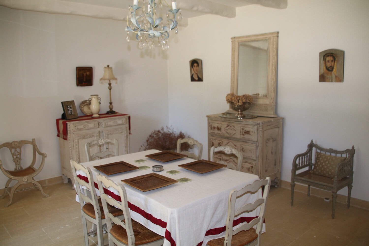 Comedor con una mesa blanca dispuesta para cuatro personas, rodeada de sillas antiguas.