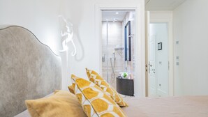 Een slaapkamer met een bed, kussens, een nachtkastje, een spiegel en een deur naar een badkamer met een douche.