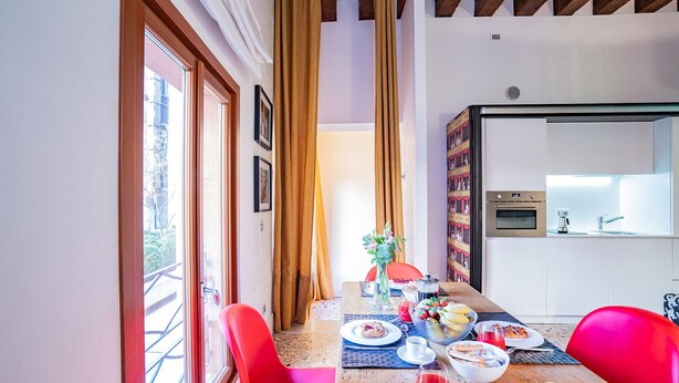 Een eetgedeelte met een houten tafel gedekt voor het ontbijt, een keuken met moderne apparatuur en een balkon met uitzicht.