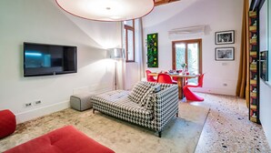 Een moderne woonkamer met een bank, een televisie, een rode fauteuil en een eethoek met een tafel en stoelen.