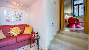 Een moderne woonkamer met een rode bank, een bijzettafeltje met een fles en een schaal fruit, en een trap die naar een andere kamer leidt.