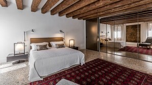 Un dormitorio moderno con una cama grande, vigas de madera, un tapete rojo con estampado y un cerrojo corredizo que da a otra habitación.