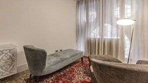 Una habitación con un sofá gris, un tapete estampado, una lámpara de pie y cortinas de gasa.