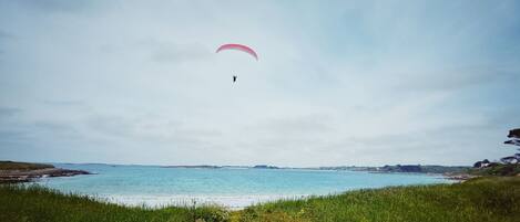 Un paisaje costero con una persona practicando parapente sobre el agua.