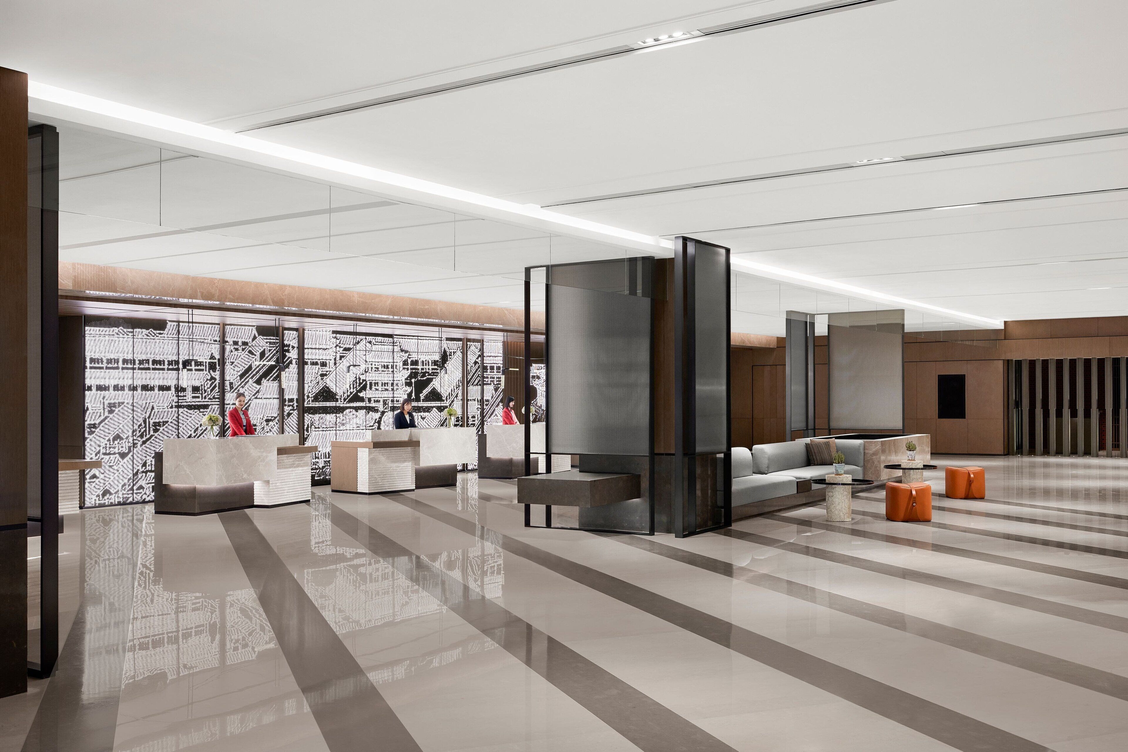 A modern lobby with a reception desk, seating area, and a large glass partition.