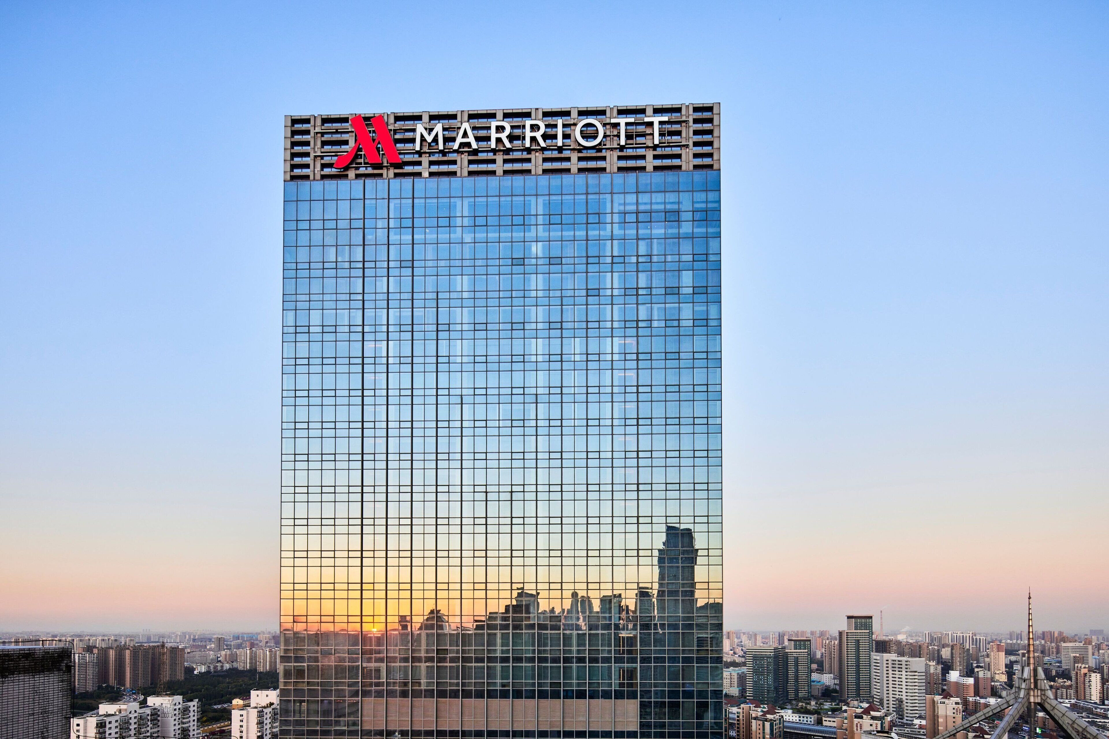 Um hotel imponente com o logotipo Marriott, apresentando uma fachada em padrão quadriculado e um horizonte urbano ao fundo.