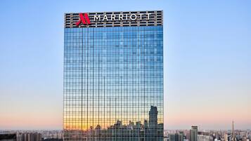 Um hotel imponente com o logotipo Marriott, apresentando uma fachada em padrão quadriculado e um horizonte urbano ao fundo.