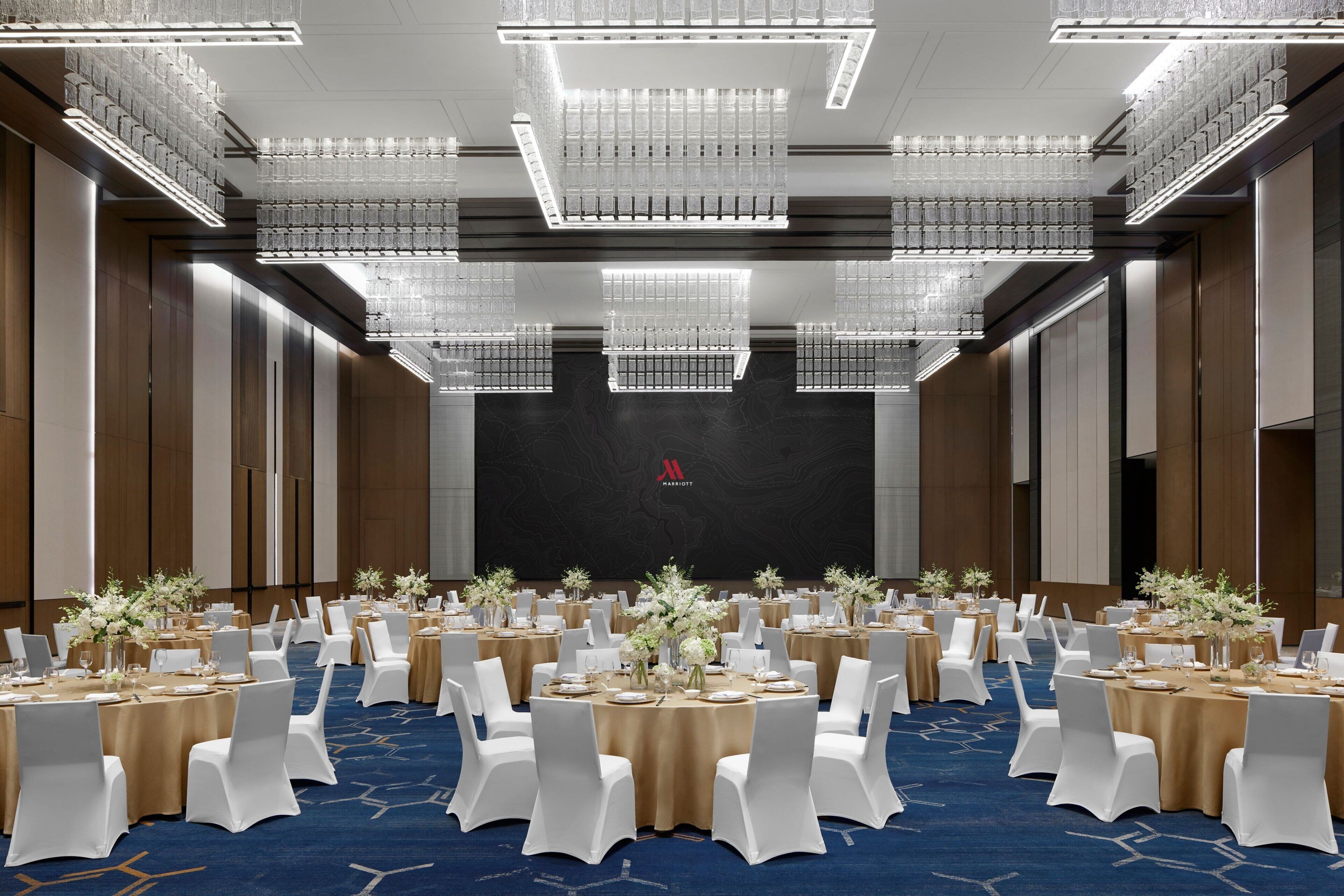 Un amplio salón de conferencias con mesas redondas, sillas blancas y candelabros.