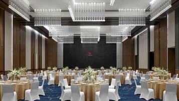 Un amplio salón de conferencias con mesas redondas, sillas blancas y candelabros.