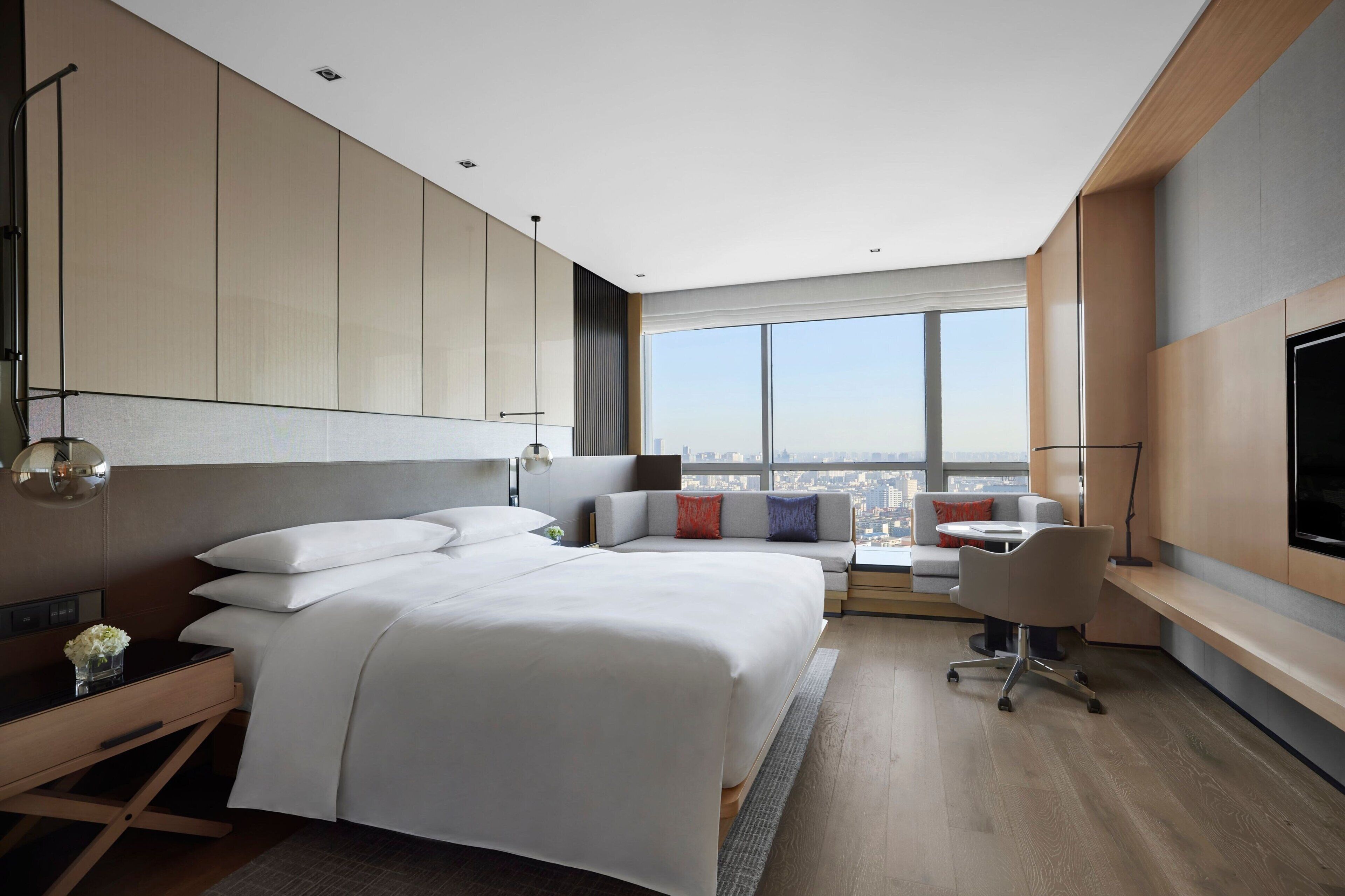 A modern hotel room with a large bed, a desk, and a view of the city.