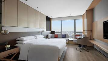 A modern hotel room with a large bed, a desk, and a view of the city.