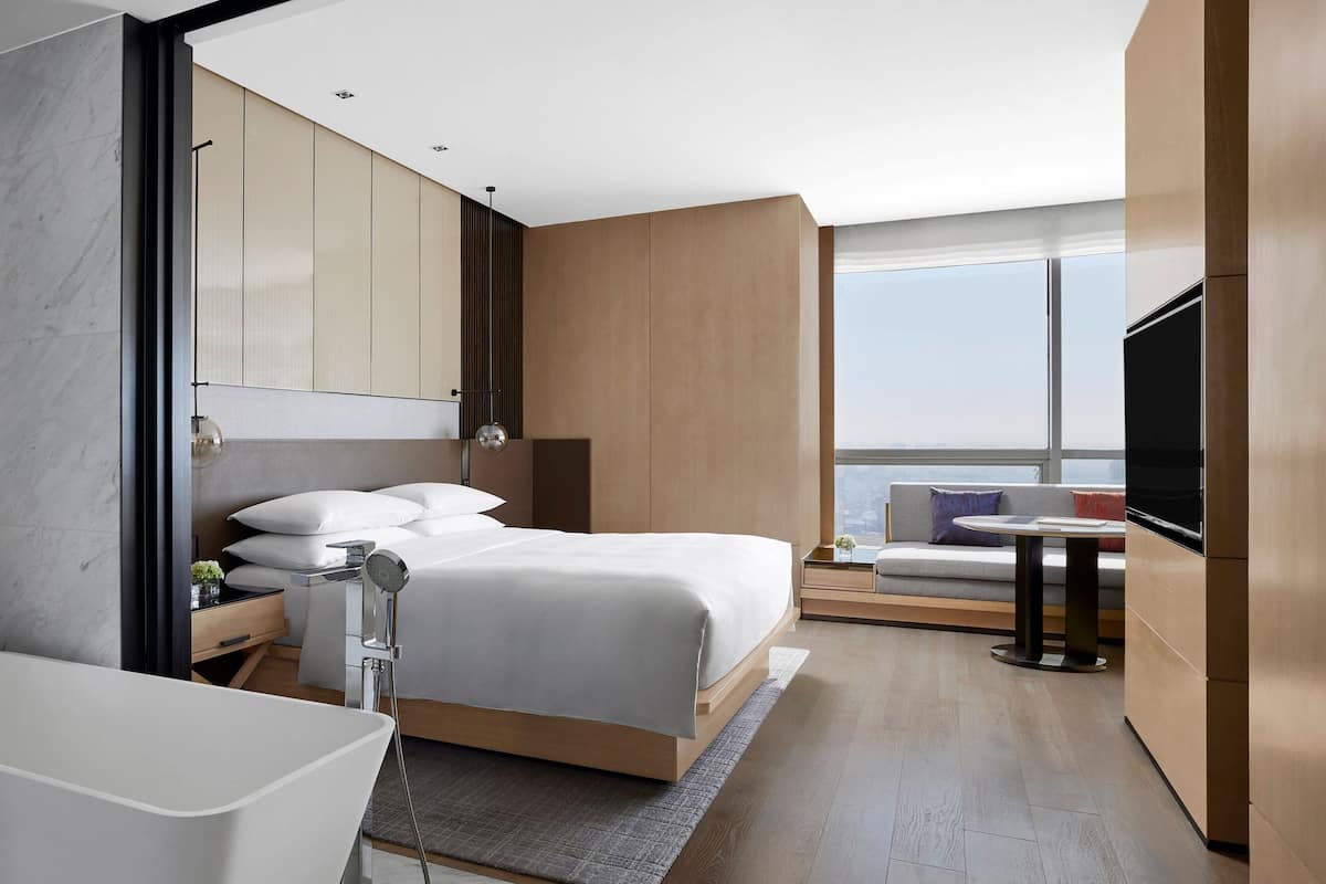 Moderni hotellihuone, jossa on suuri sänky, erillinen kylpyhuone, pieni pöytä ja näkymä kaupunkiin.