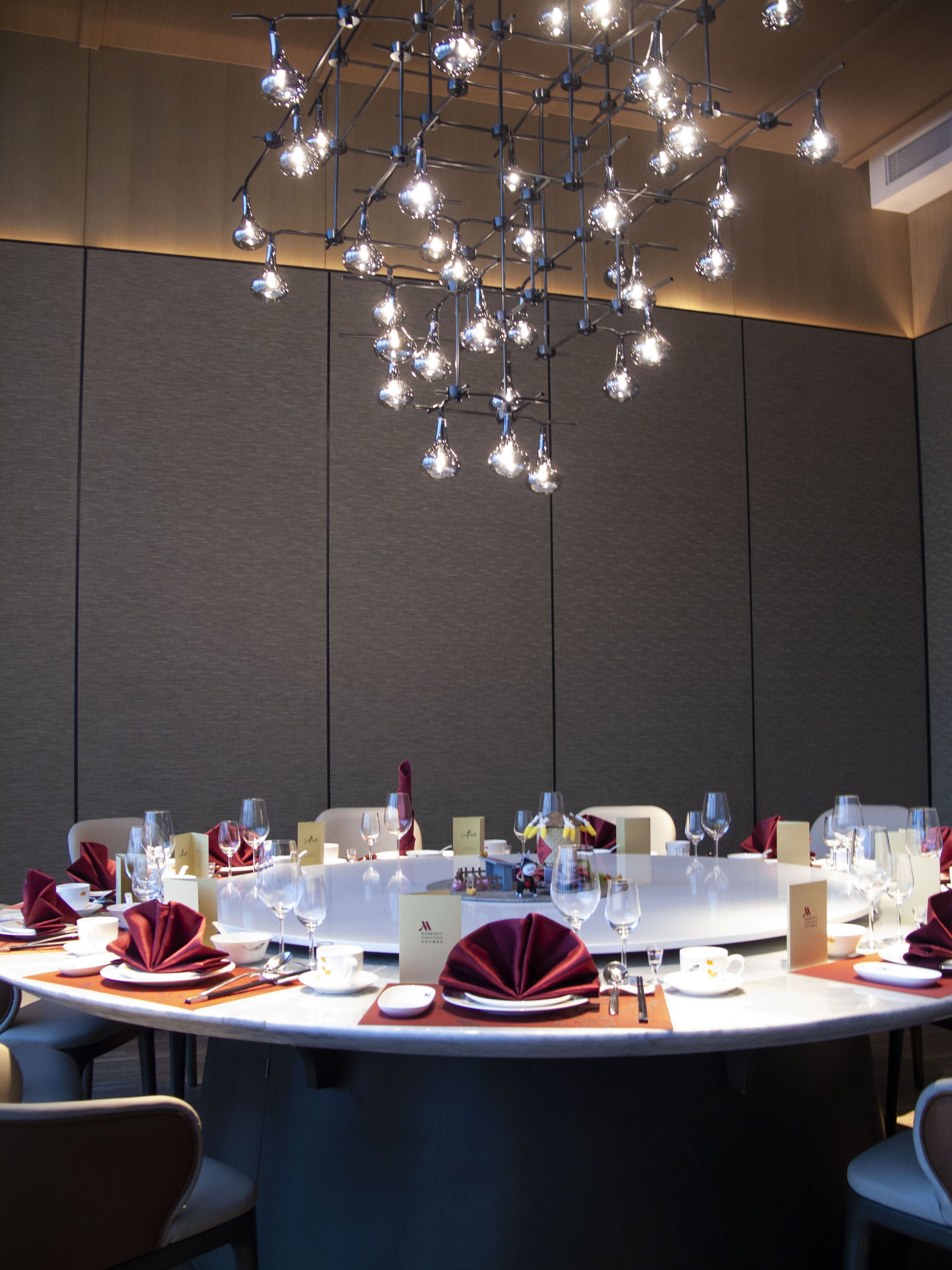 A conference room with a round table set for a meeting, equipped with nameplates, chairs, and a modern chandelier.