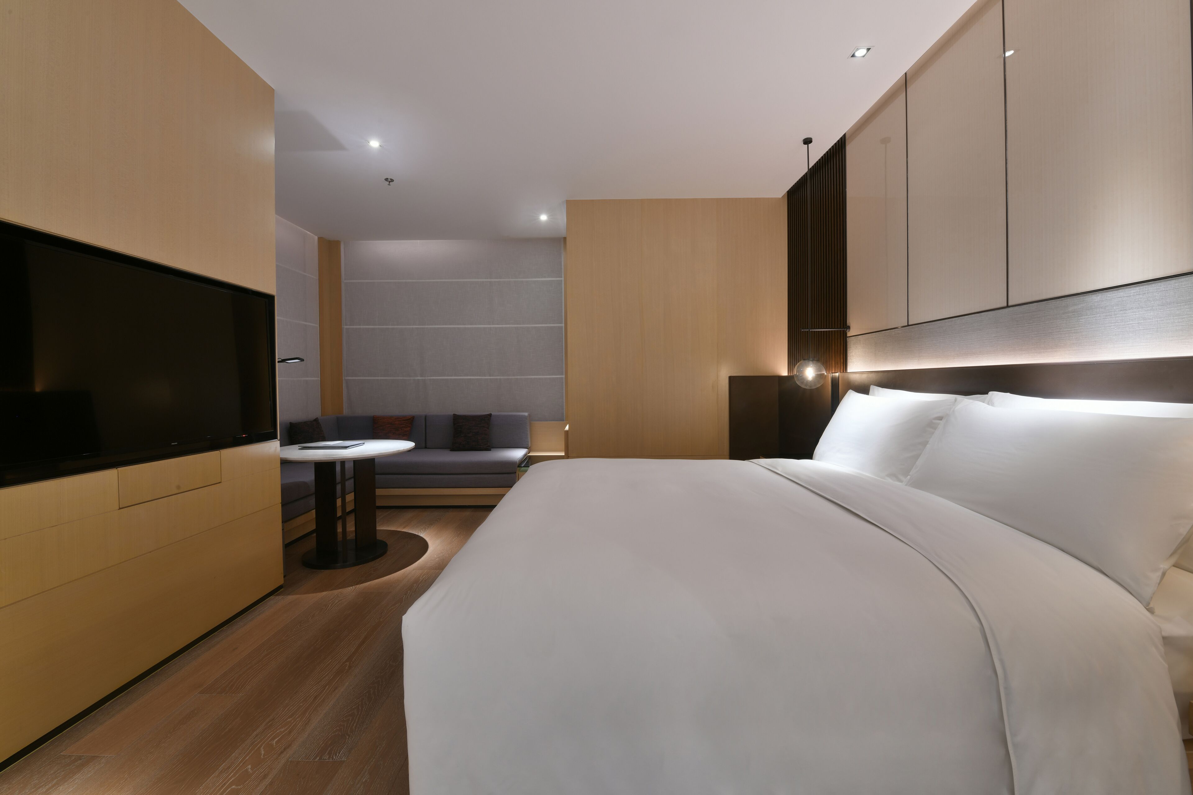A modern hotel room with a large bed, a flat-screen TV, a small round table, and a sofa.