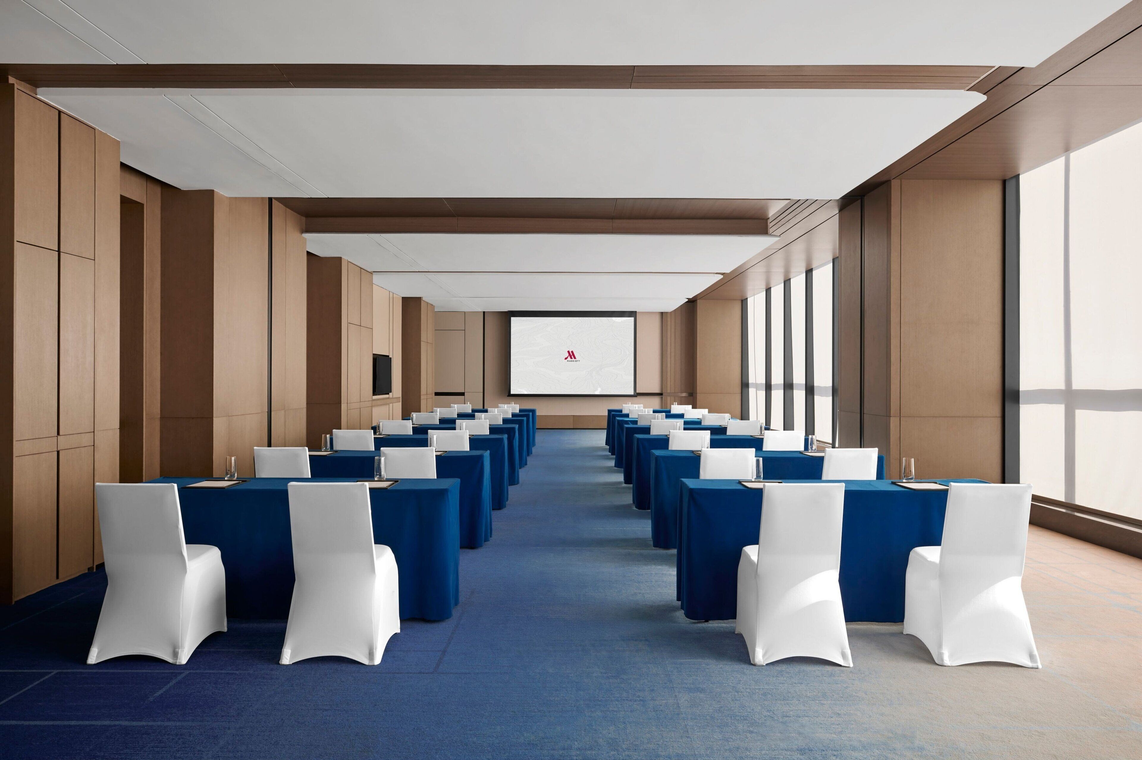 A conference room with rows of tables and chairs, a projector screen, and large windows.