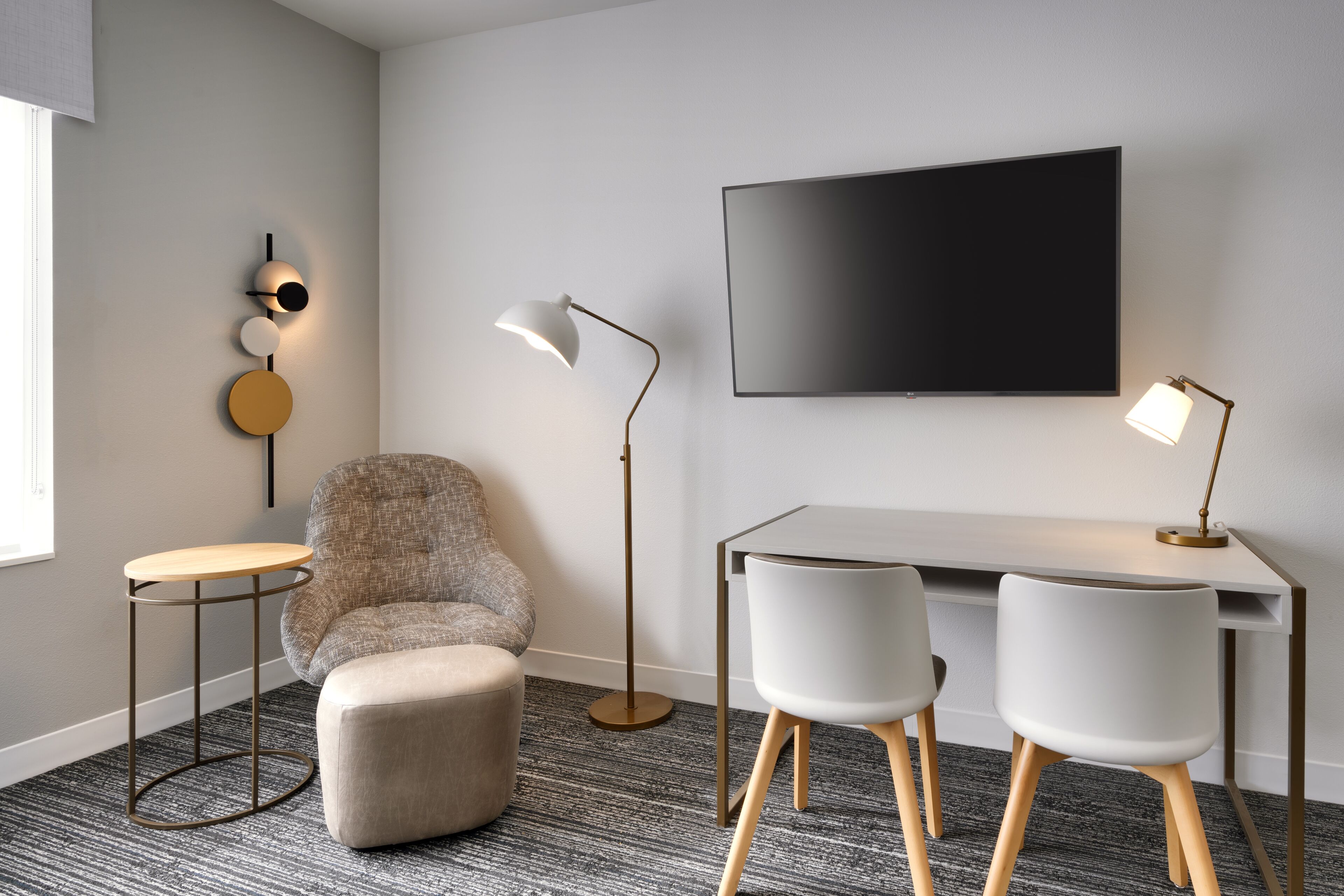 A modern room with a flat-screen TV, two chairs, a round table, a sofa, and two floor lamps.