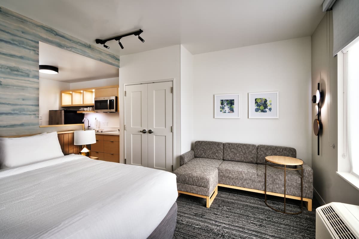 Ein Hotelzimmer mit einem Bett, einer Couch, einem kleinen Tisch, einer Mikrowelle, einer Tür und Bildern an der Wand.