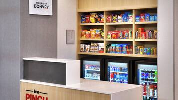 Zona de venta de aperitivos y bebidas en un hotel Marriott Bonvoy, con varias estanterías llenas de snacks y dos refrigeradores provistos de bebidas.