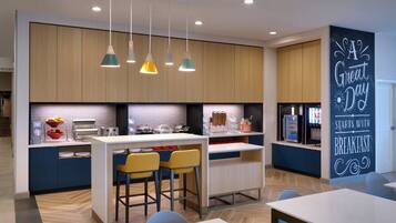 A modern kitchen with a central island, bar stools, pendant lighting, and a wall sign.