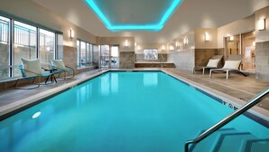 A modern indoor swimming pool with clear blue water, surrounded by lounge chairs and a glass wall with windows. - TownePlace Suites by Marriott Salt Lake City Murray (Murray)