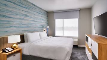 Une chambre d’hôtel avec un lit, une table de chevet avec une lampe, une télévision et une fenêtre donnant sur un beau paysage.