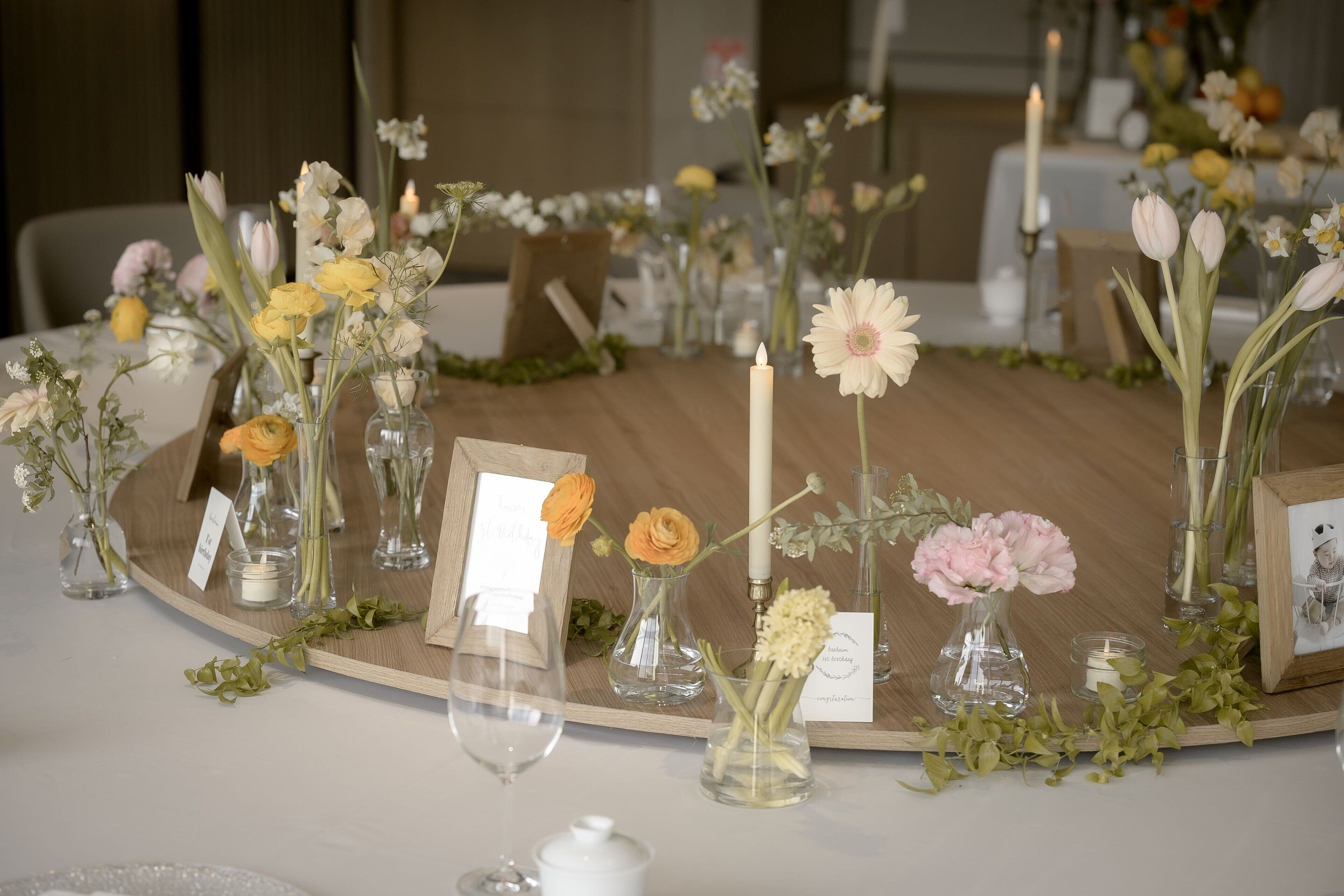 A round table with floral centerpieces, candles, and small vases.