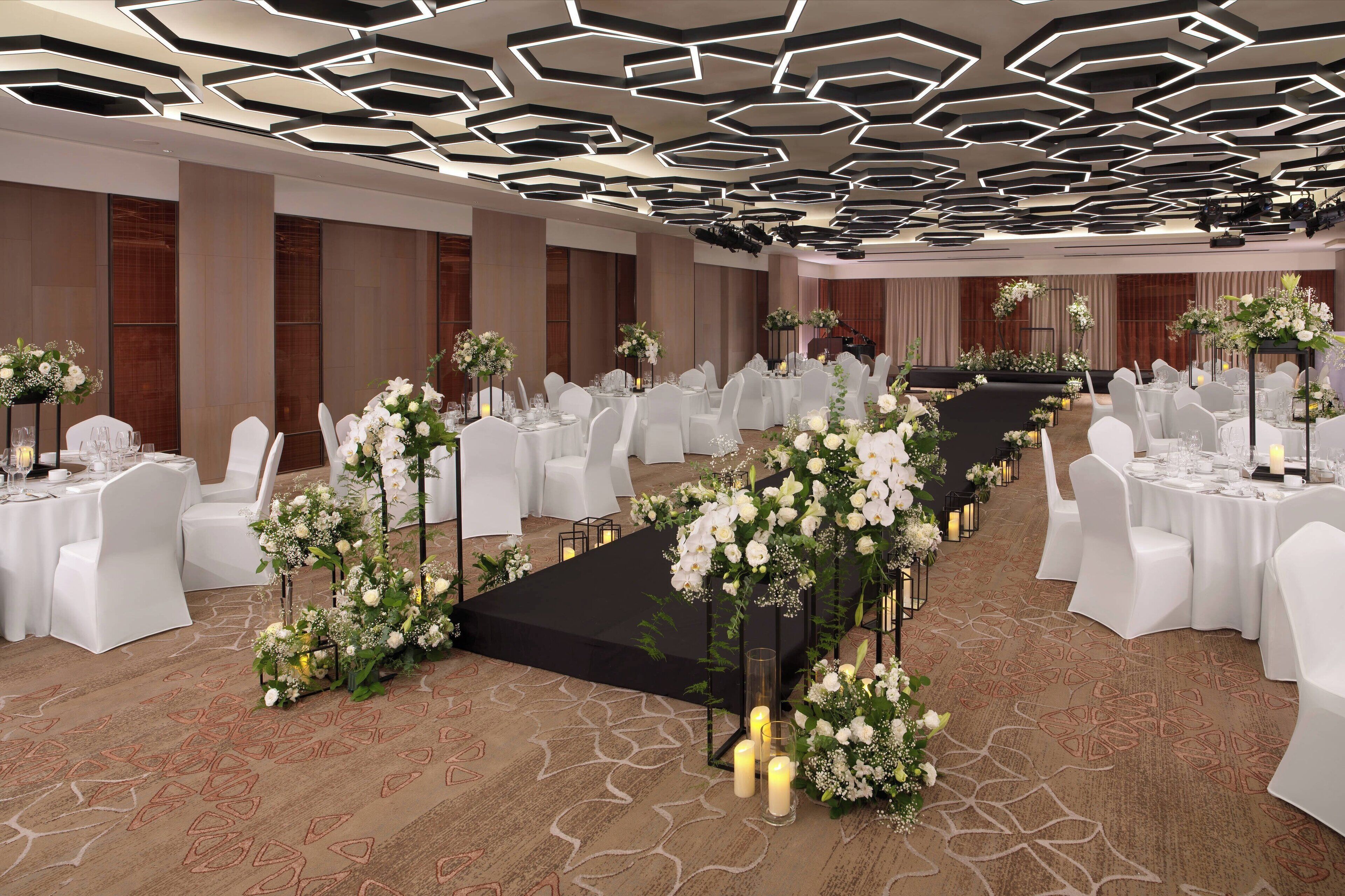 A banquet hall with white chairs and tables, floral centerpieces, and a black aisle.