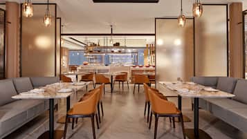 A modern dining area with tables and chairs, a central bar area, and a seating area with sofas.