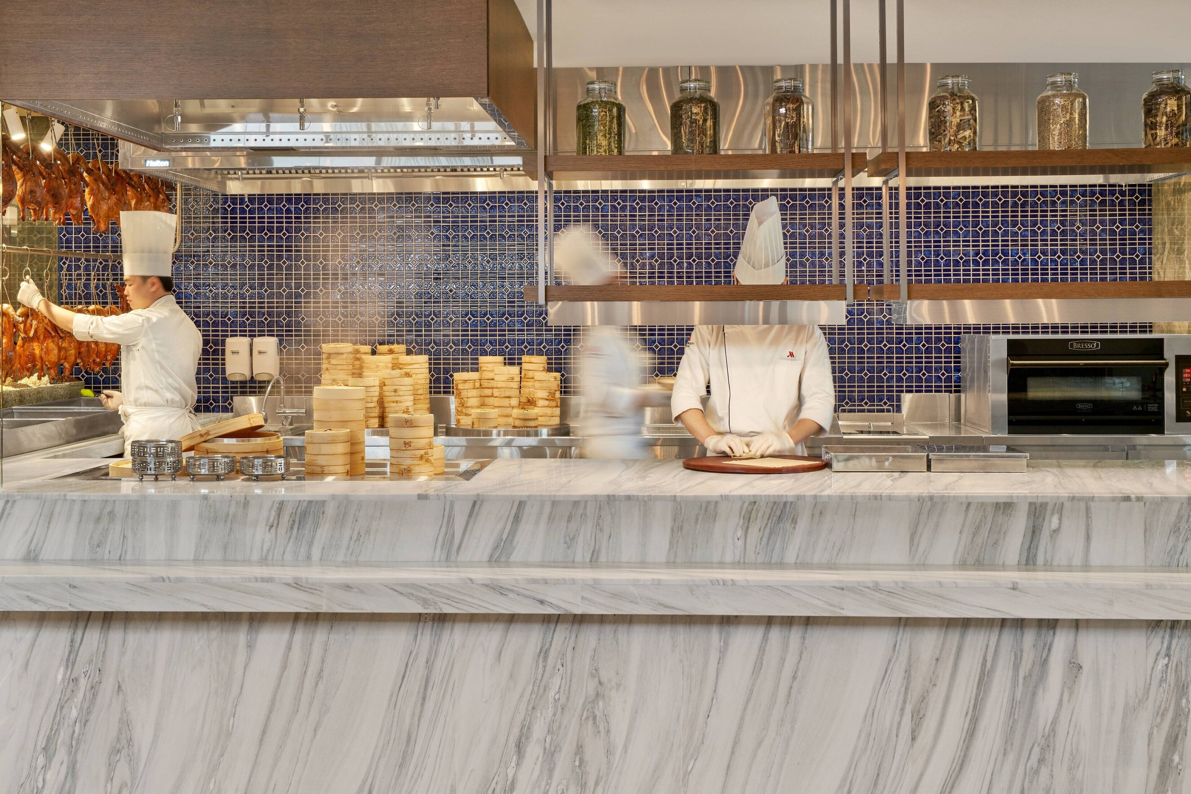 A modern kitchen with marble countertops, a blue tiled backsplash, and stainless steel appliances.