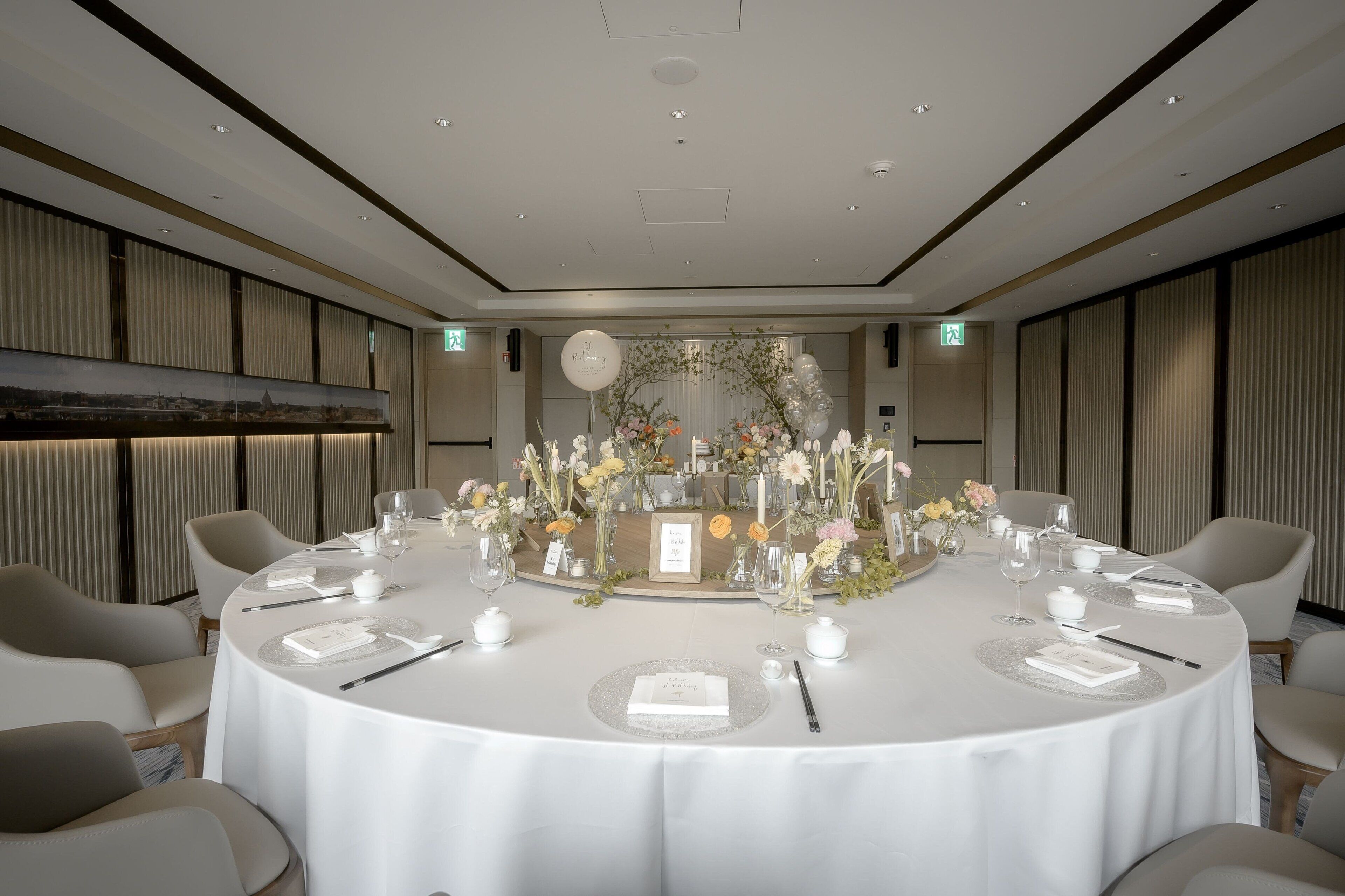 Una mesa redonda de comedor con manteles blancos, centros de mesa florales y sillas modernas.