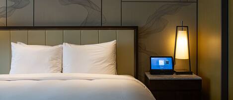 A hotel room with a bed, a nightstand with a lamp, and a laptop.