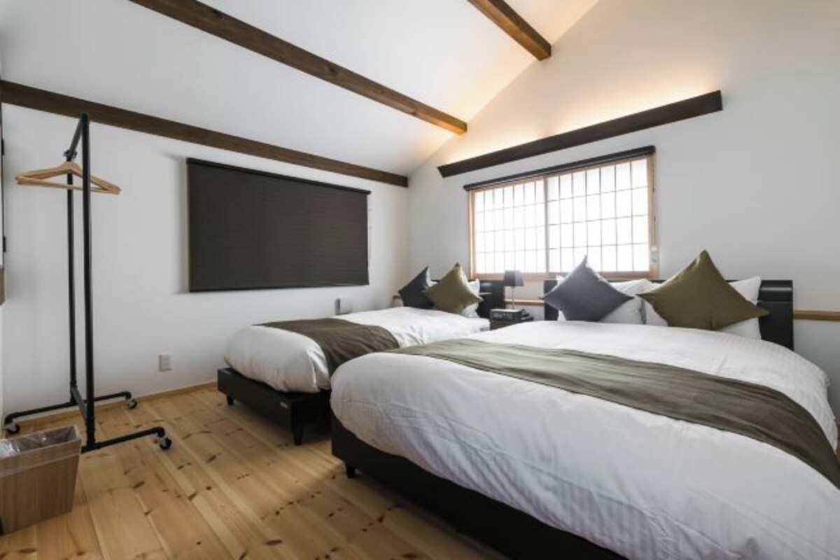 A bedroom with two beds, a large window, and a blackboard on the wall.