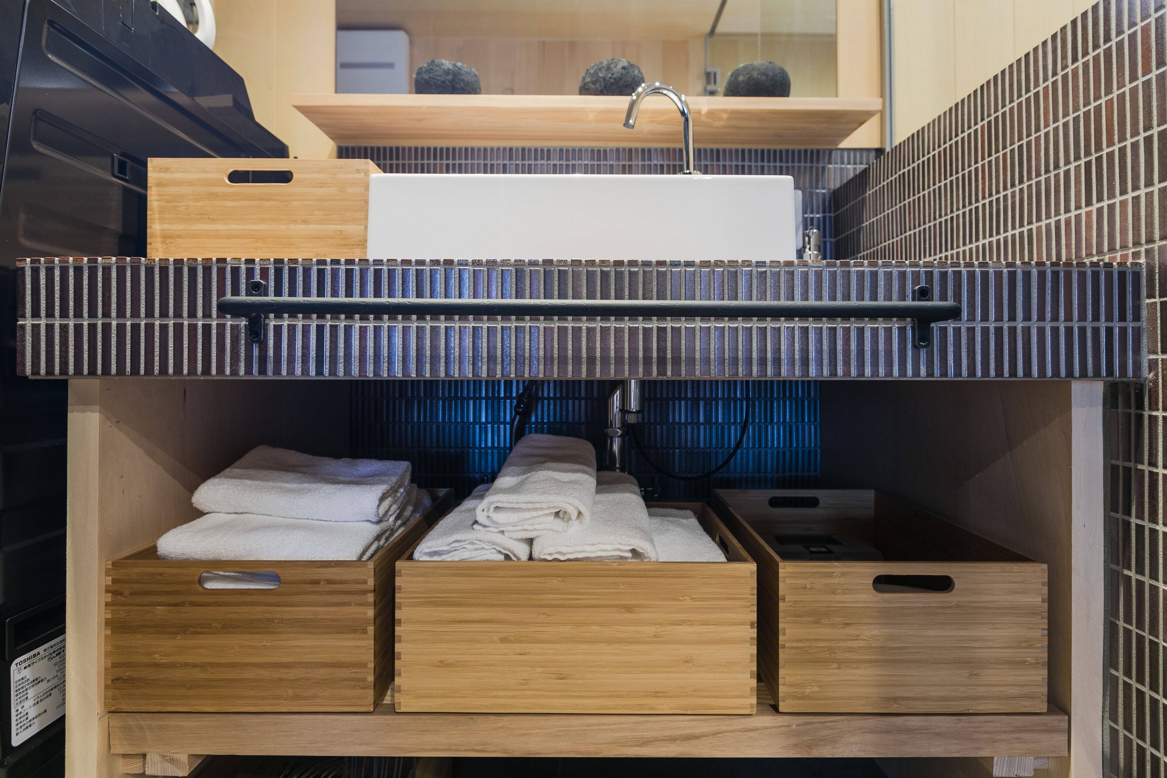 A compact bathroom with a built-in sink, wooden storage drawers, and a tiled backsplash.