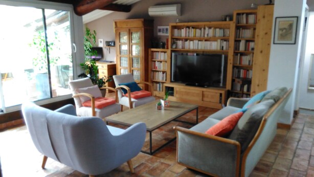 A living room with a sofa, armchairs, a coffee table, and a TV. There are bookshelves and a plant. - Town center with terrace (Aix-en-Provence)
