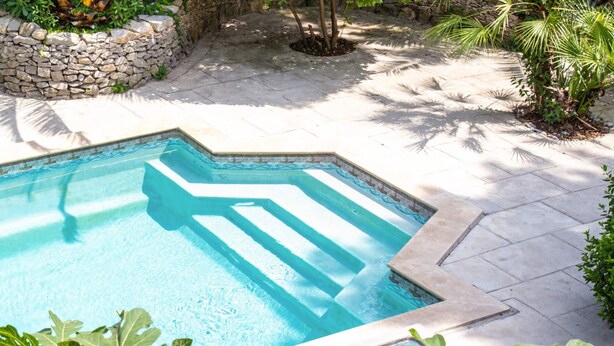 A swimming pool with a stone border, surrounded by a stone wall and plants.