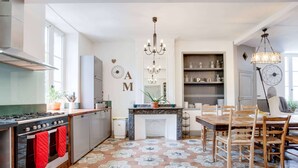 A modern kitchen with a gas stove, oven, and red oven mitts hanging on the oven door. There is a dining table with chairs and a chandelier above it.