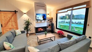 A modern living room with a fireplace, a television, and a large window overlooking a pool. - VILLA OASIS : Ideal for families and groups. (Arcos De La Frontera)