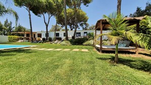 A poolside area with a grassy lawn, lounge chairs, a wooden pergola, and a thatched-roof structure. - VILLA OASIS : Ideal for families and groups. (Arcos De La Frontera)