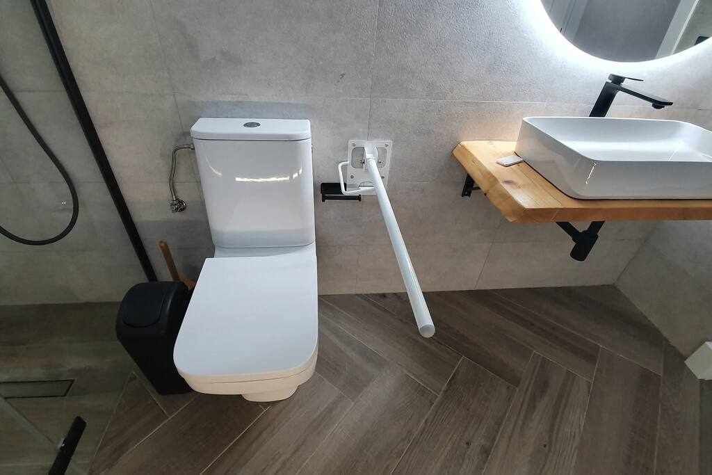 A modern bathroom with a white toilet, a wooden vanity with a sink, and a shower area.