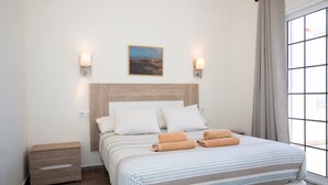 Un dormitorio ordenado con una cama grande, dos mesitas de noche, un cuadro en la pared y dos apliques.