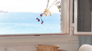 Una mesa de comedor con una cesta encima, dos sillas blancas y vista al mar a través de una ventana.