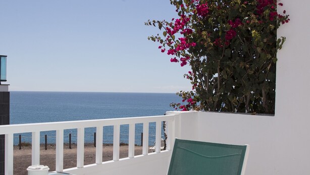 Un balcón con barandal blanco, una mesa con una silla verde y vista al mar.