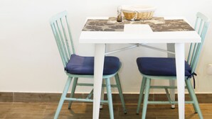 A dining area with a white table, two teal chairs, a wicker basket, and a framed picture on the wall. - VM7, first floor. (El Cotillo)