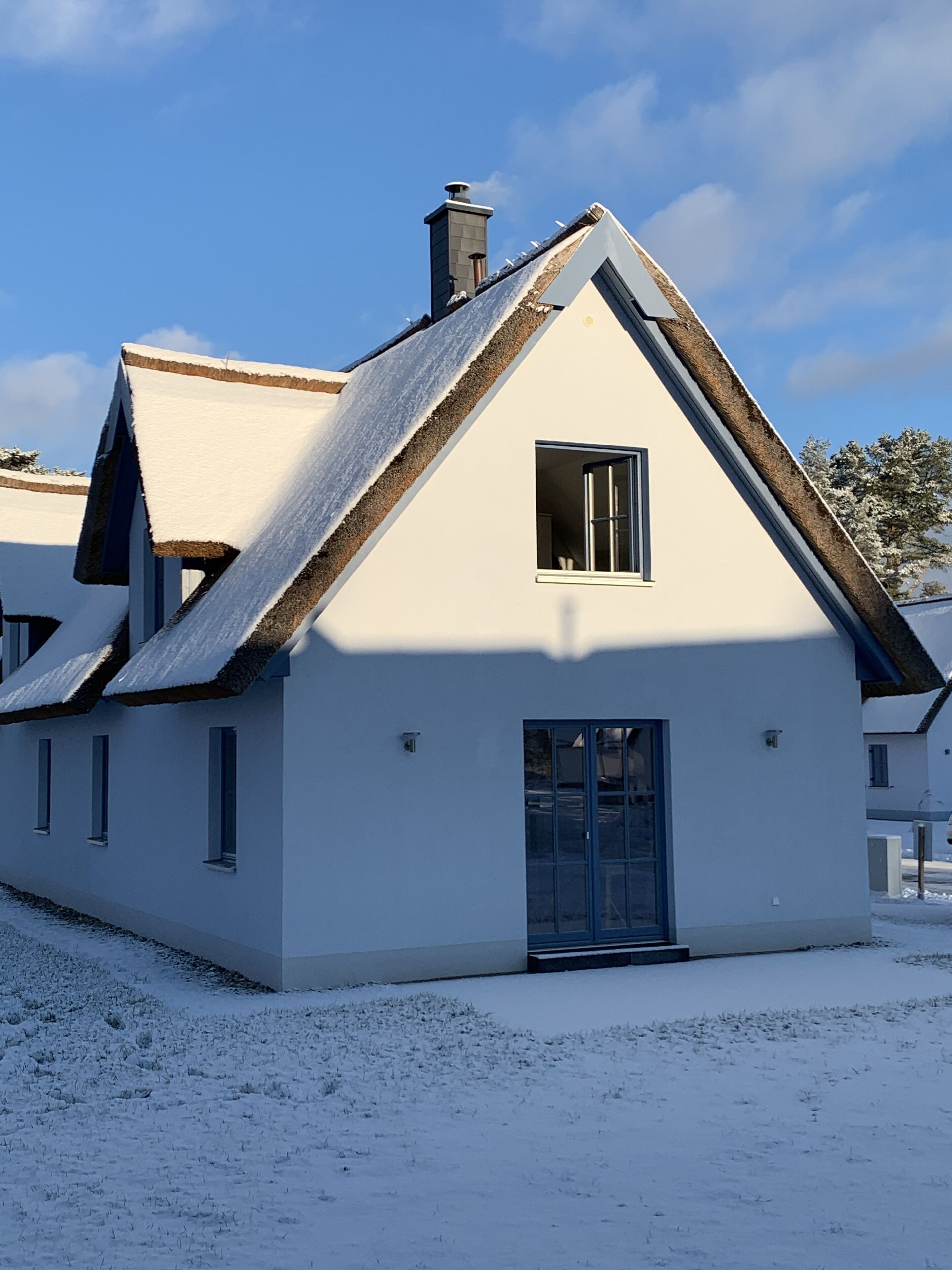 A white building with a steeply pitched roof, a chimney, and a window.