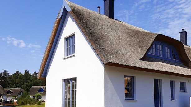 Una casa blanca con techo de paja y chimenea, rodeada de césped.