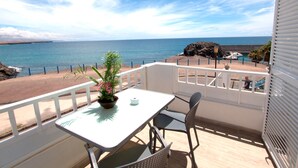 Un balcón con una mesa y sillas, con vista a la playa y al mar.